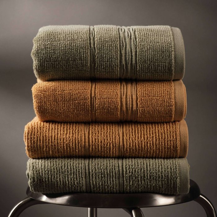Folded bath towels in ochre, olive and charcoal, stacked on a chair